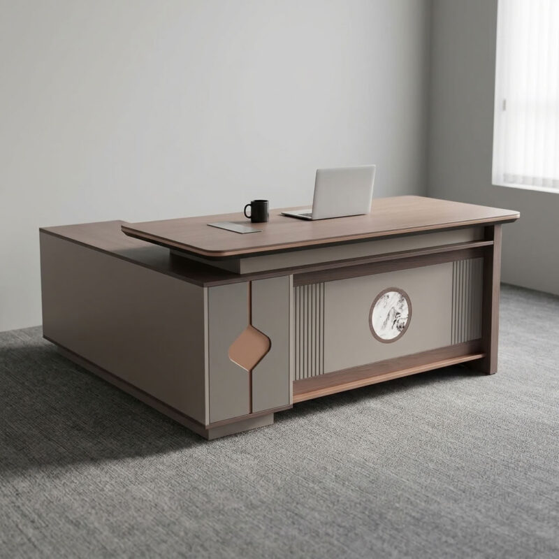 1.8m executive office table featuring a walnut wood grain laminate desktop with bevel-trimmed edges and grey side paneling, an L-shaped return cabinet structure with integrated storage compartments, a front modesty panel with fluted detailing and a central decorative emblem, built-in desktop flip-top cable management grommet, and a heavy-duty full-plinth base with floor-protective glides.