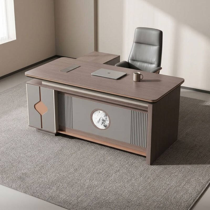 1.8m executive office table featuring a walnut wood grain laminate desktop with bevel-trimmed edges and grey side paneling, an L-shaped return cabinet structure with integrated storage compartments, a front modesty panel with fluted detailing and a central decorative emblem, built-in desktop flip-top cable management grommet, and a heavy-duty full-plinth base with floor-protective glides.