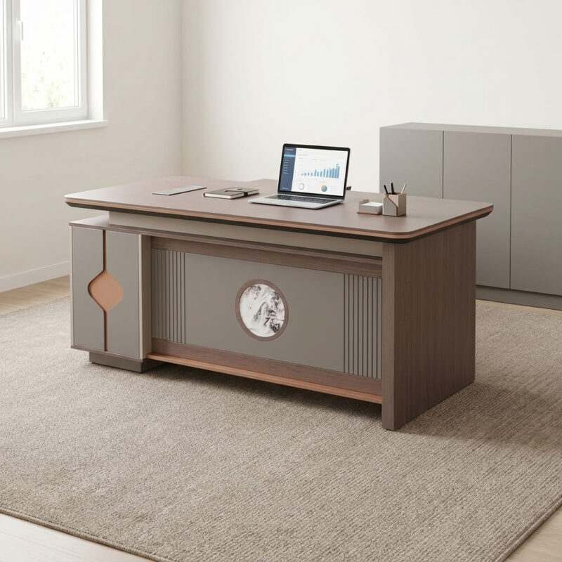 1.8m executive office table featuring a walnut wood grain laminate desktop with bevel-trimmed edges and grey side paneling, an L-shaped return cabinet structure with integrated storage compartments, a front modesty panel with fluted detailing and a central decorative emblem, built-in desktop flip-top cable management grommet, and a heavy-duty full-plinth base with floor-protective glides.